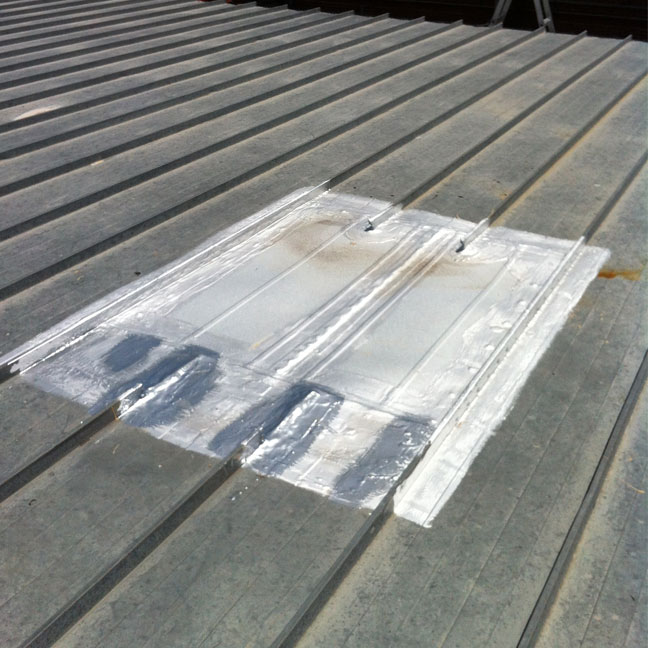 Flat metal panel with stiffening ribs installed after a roof curb was removed and left a hole in the standing seam roof.